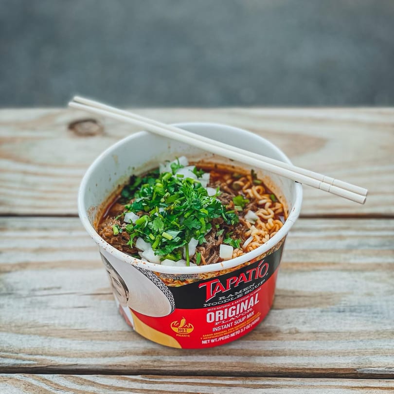 Tapatio ramen noodle soup with beef, cilantro, and diced onions, with chopsticks on top.