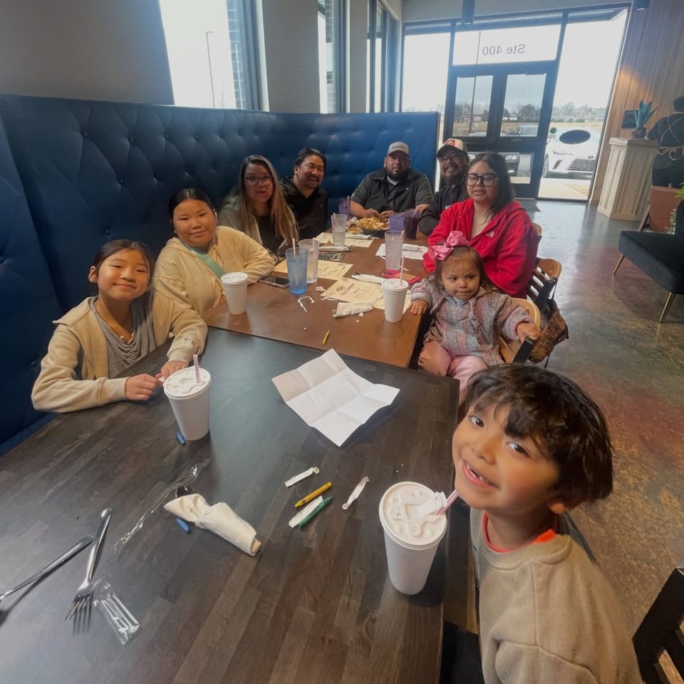 A large family group, including children, seated at tables in a brightly lit Los Compas Margaritatown restaurant.