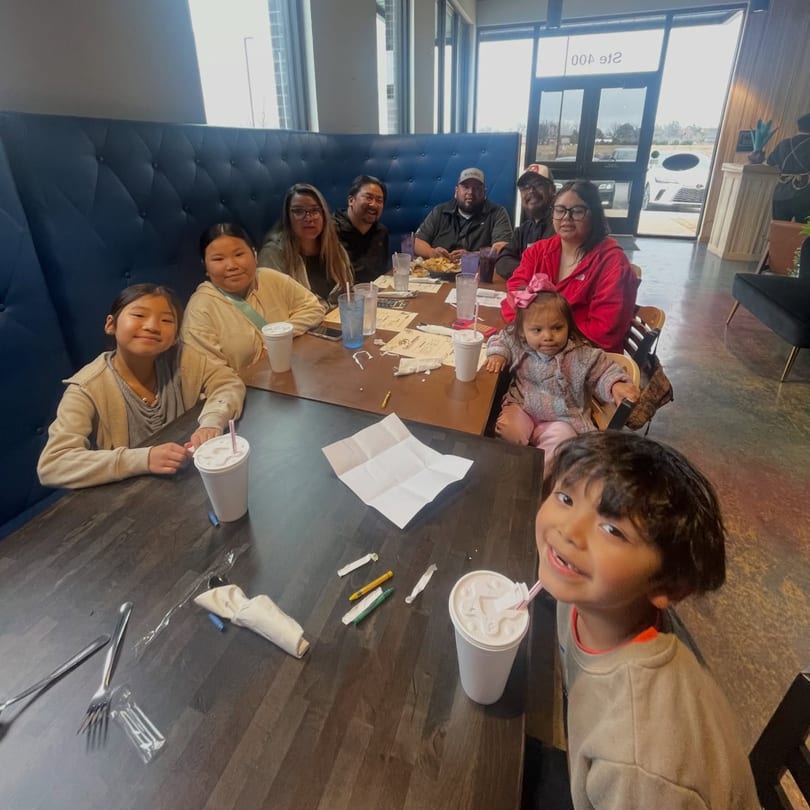 A large family group, including children, seated at tables in a brightly lit Los Compas Margaritatown restaurant.
