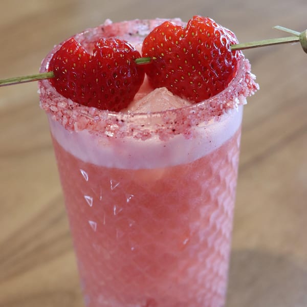 Close-up of a pink strawberry margarita with a sugar-rimmed glass and two fresh strawberries.