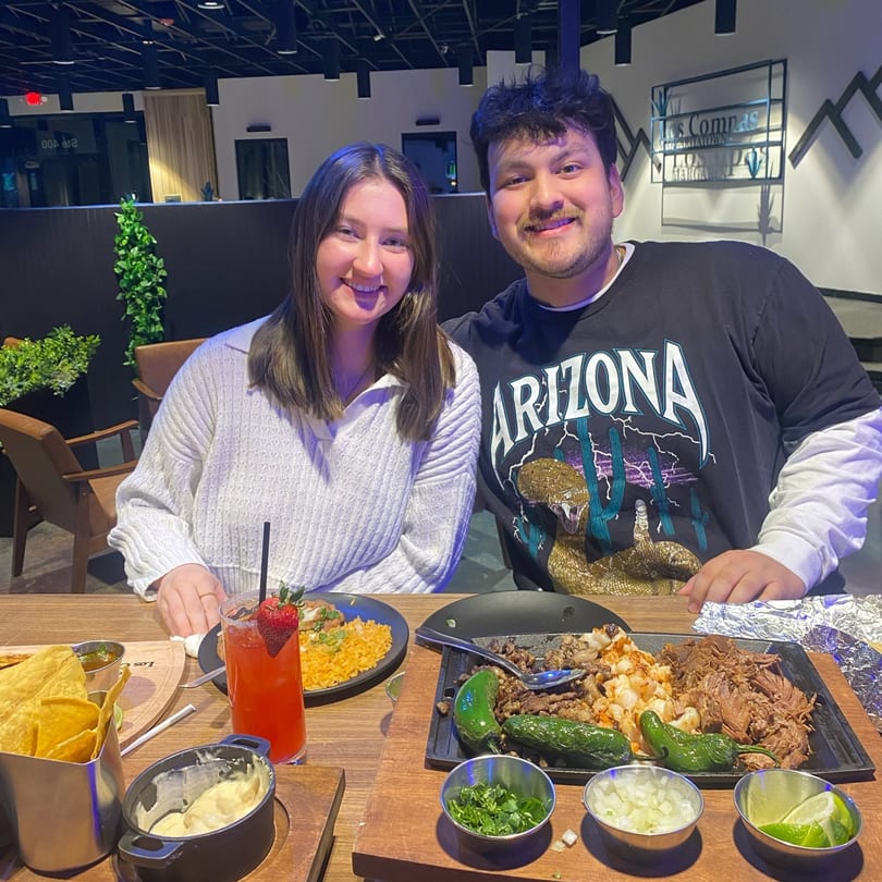 Smiling couple at Los Compas Margaritatown with Mexican food, drinks, and chips on their table.