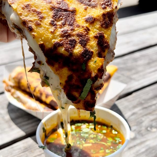 A cheesy birria quesadilla from Los Compas Margaritatown, dripping into a cup of consommé.