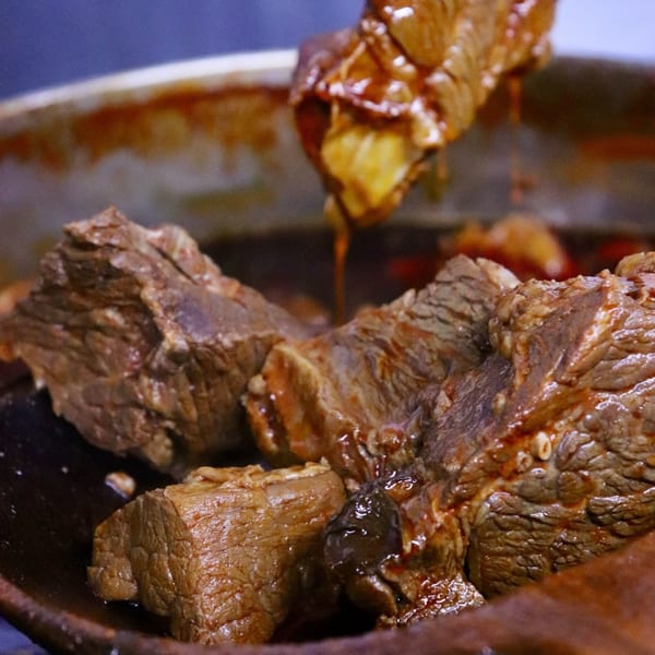 Close-up of tender, saucy Mexican birria beef being lifted from a pot.